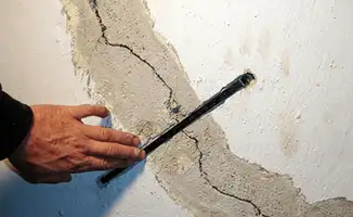 A wall with a large crack is being inspected by a professional in Tacoma, WA